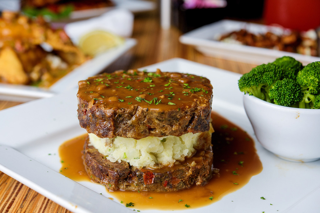 Two slices of homemade meatloaf are layered with garlic mashed potatoes and covered with hot onion gravy.