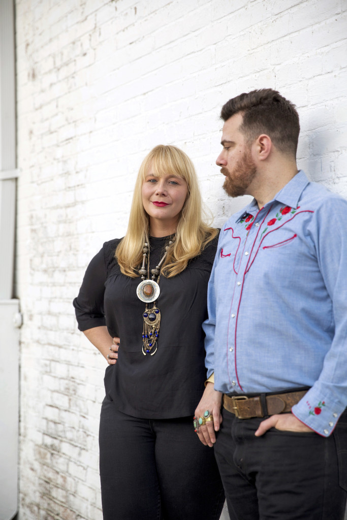 Swetman wears her own ’60s-style black shirt and pants paired with a statement necklace from Time Warp. She found her rings and layered necklaces at various estate sales. Anselmo wears a rockabilly-style denim shirt from Time Warp paired with his own jeans and leather belt. 