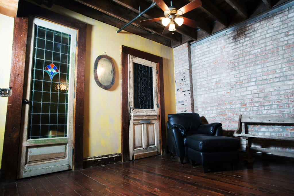 The living room is characterized by weathered wood flooring and exposed brick walls and ceiling beams. An old church pew provides seating.