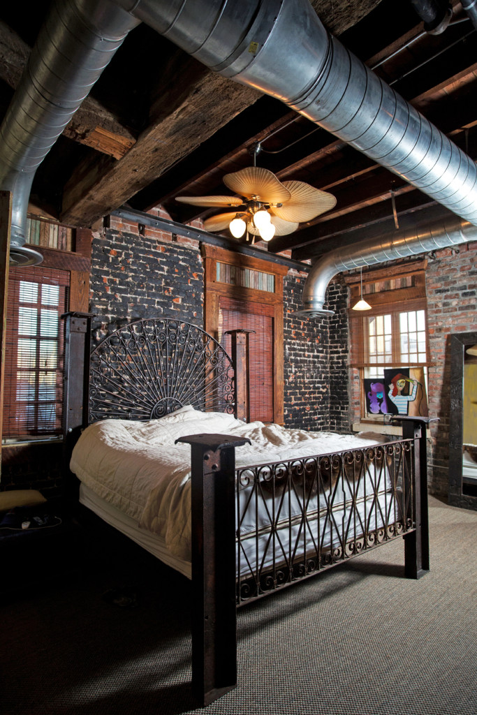 An iron bed frame and headboard align perfectly with the apartment’s industrial feel. The exposed brick wall was partially painted black for a charred look.