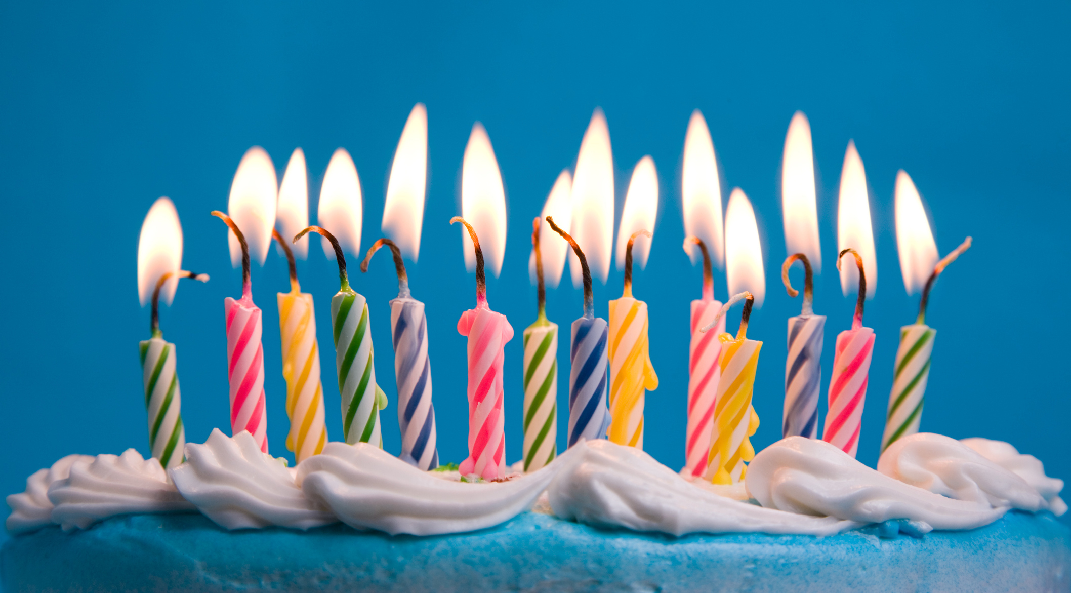 boy-blowing-out-candles-on-a-birthday-cake-against-blue-background