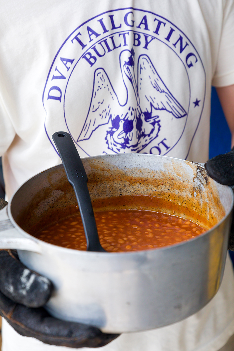 Close up of man holding large pot of baked beans with DVA tailgating t-shirt on.